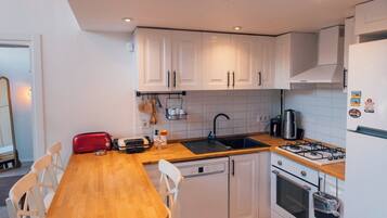 A compact kitchen with white cabinets, a wooden dining table, and a built-in oven.