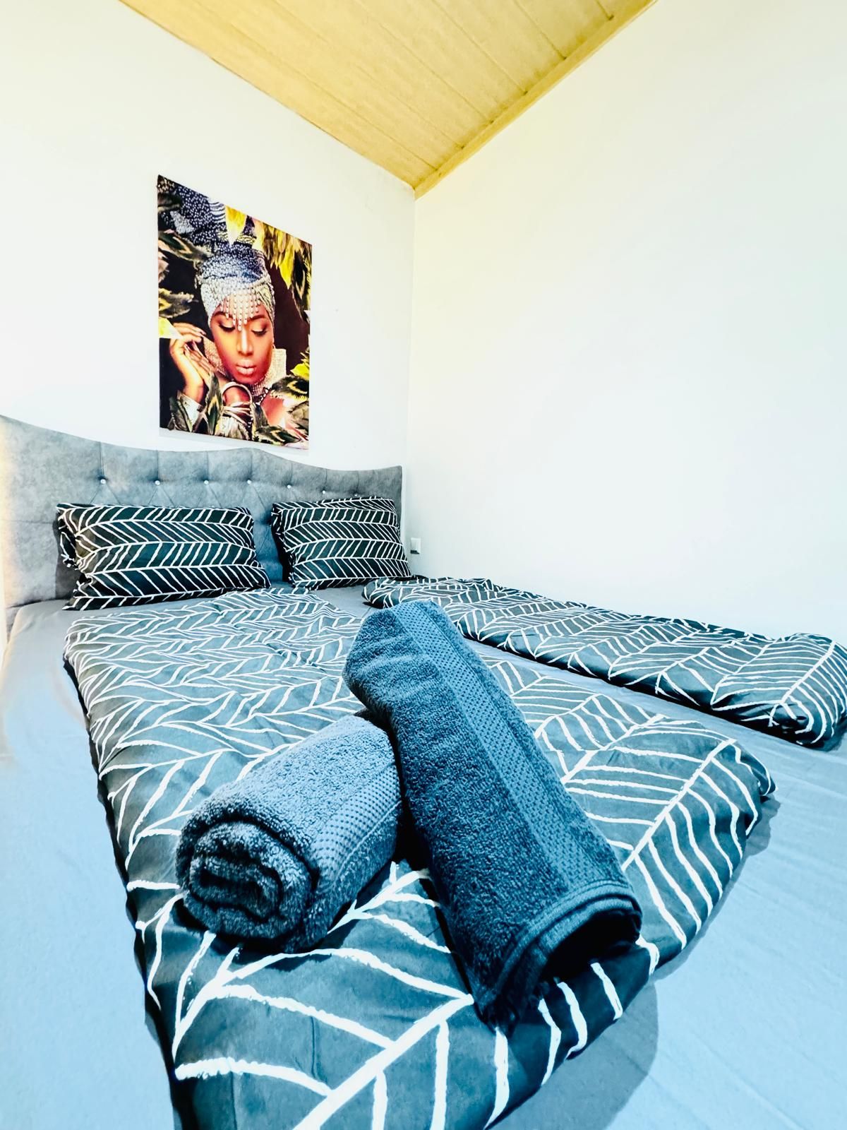 Ein Schlafzimmer mit grau gestepptem Kopfteil, gemusterten Betttextilien und einem großen gerahmten Bild an der Wand.