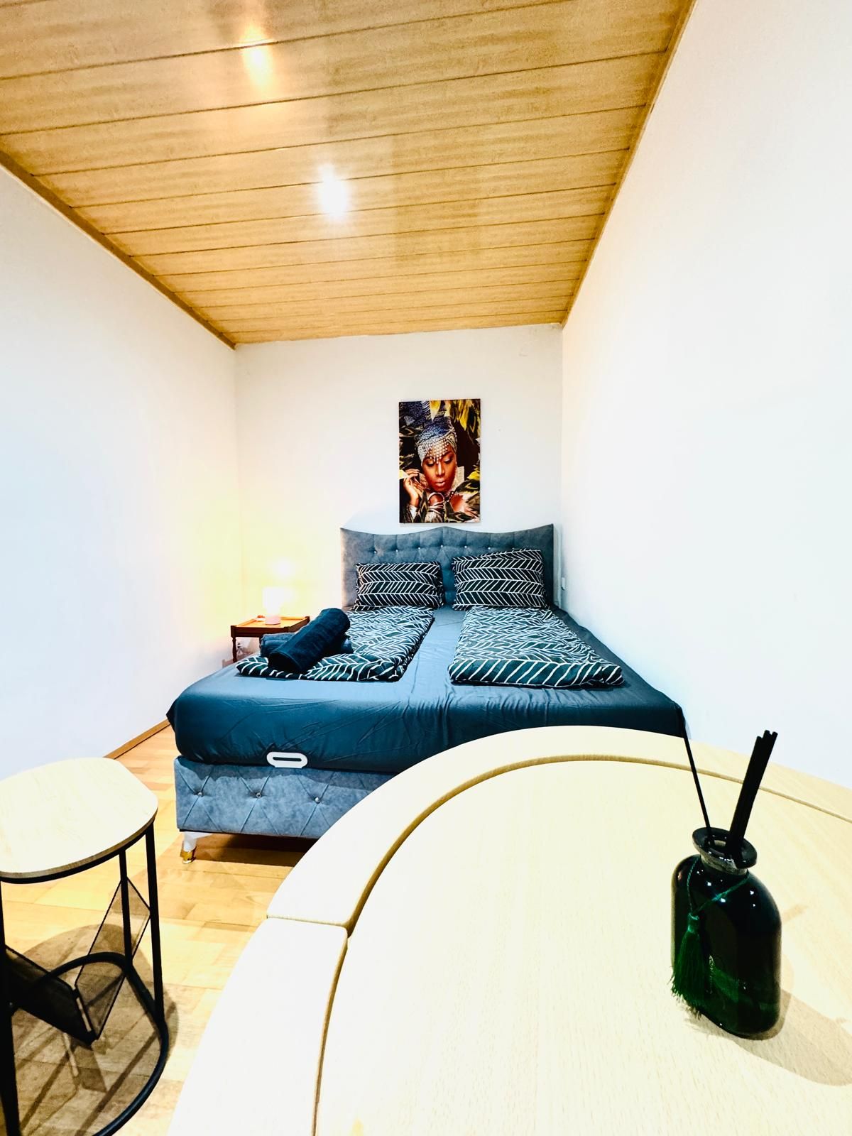 Ein Schlafzimmer mit einem Bett, einem kleinen Tisch und einer grünen Flasche auf einem weißen Tisch.