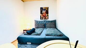 Ein Schlafzimmer mit einem Bett, einem kleinen Tisch und einer grünen Flasche auf einem weißen Tisch.