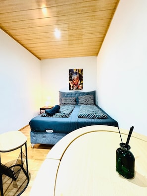 Une chambre à coucher avec un lit, une petite table et une bouteille verte posée sur une table blanche.