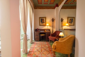 Ein Hotelzimmer mit Schreibtisch, zwei Stühlen, einem gemusterten Teppich und einem großen Spiegel.