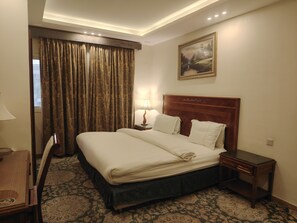 A hotel room with a large bed, a nightstand, a lamp, a painting on the wall, and a patterned carpet. - kyan Aleen Alrabwa suites (Abha)