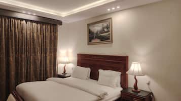 Una habitación de hotel con una cama grande, dos mesitas de noche con lámparas, un cuadro en la pared y una ventana con cortinas.