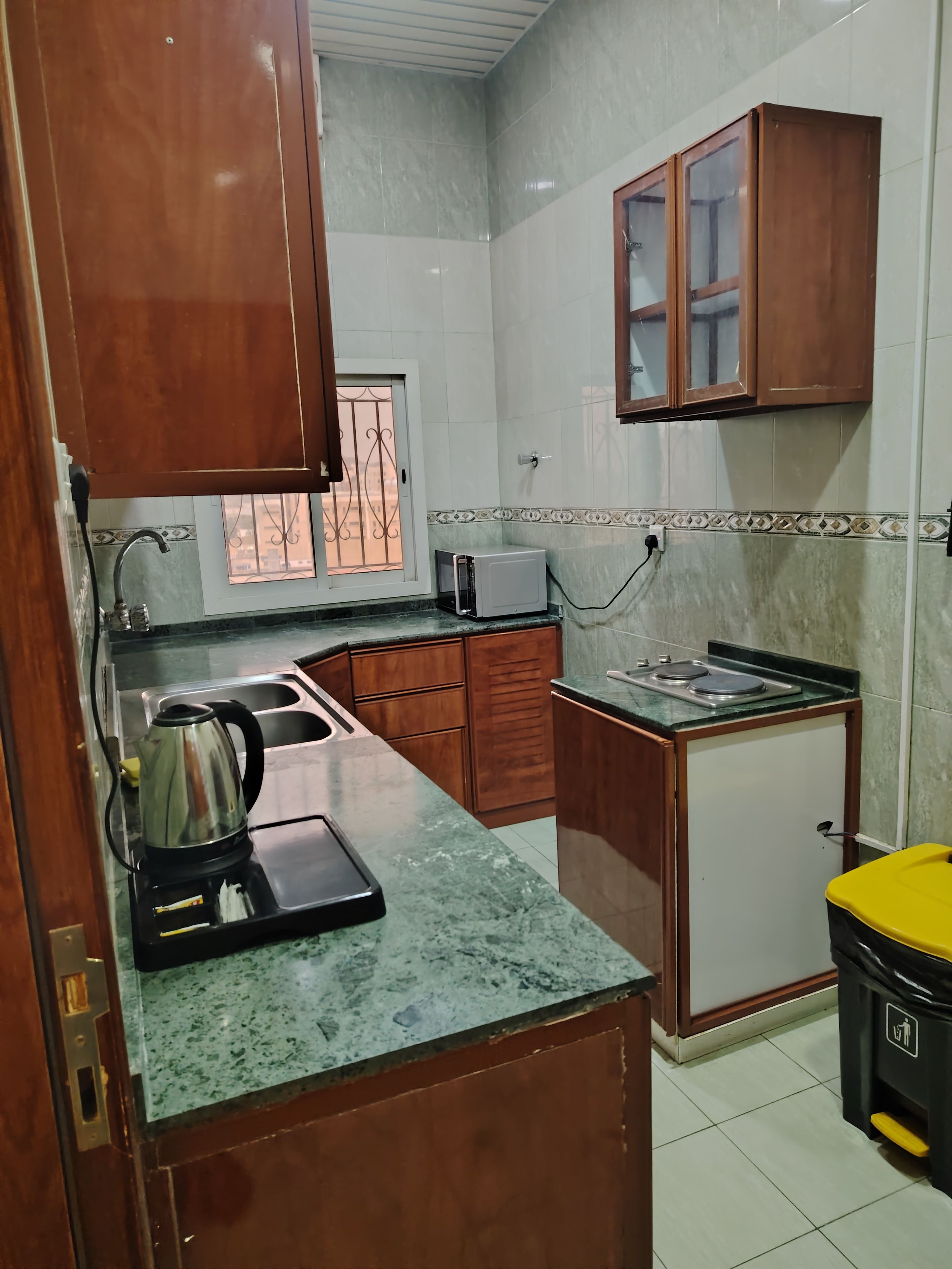 Cocina pequeña con pileta, estufa, microondas y tetera sobre la encimera.