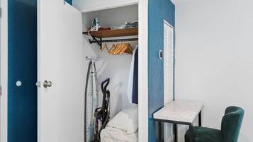 A room with a bed, a table, and a chair. There is a closet with clothes and a bicycle.