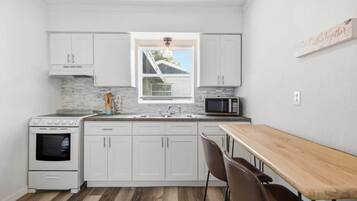A compact kitchen with white cabinets, a microwave, an oven, and a dining table with chairs.