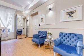 A hotel room with a mirrored wardrobe, two blue upholstered chairs, a small side table with a vase of flowers, and framed artwork on the walls. - Muzio Private Suites by Premium Suites Collection (ROME)