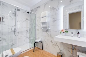 A modern bathroom with a glass-enclosed shower, a toilet, a sink with a mirror, and a small stool. - Muzio Private Suites by Premium Suites Collection (ROME)