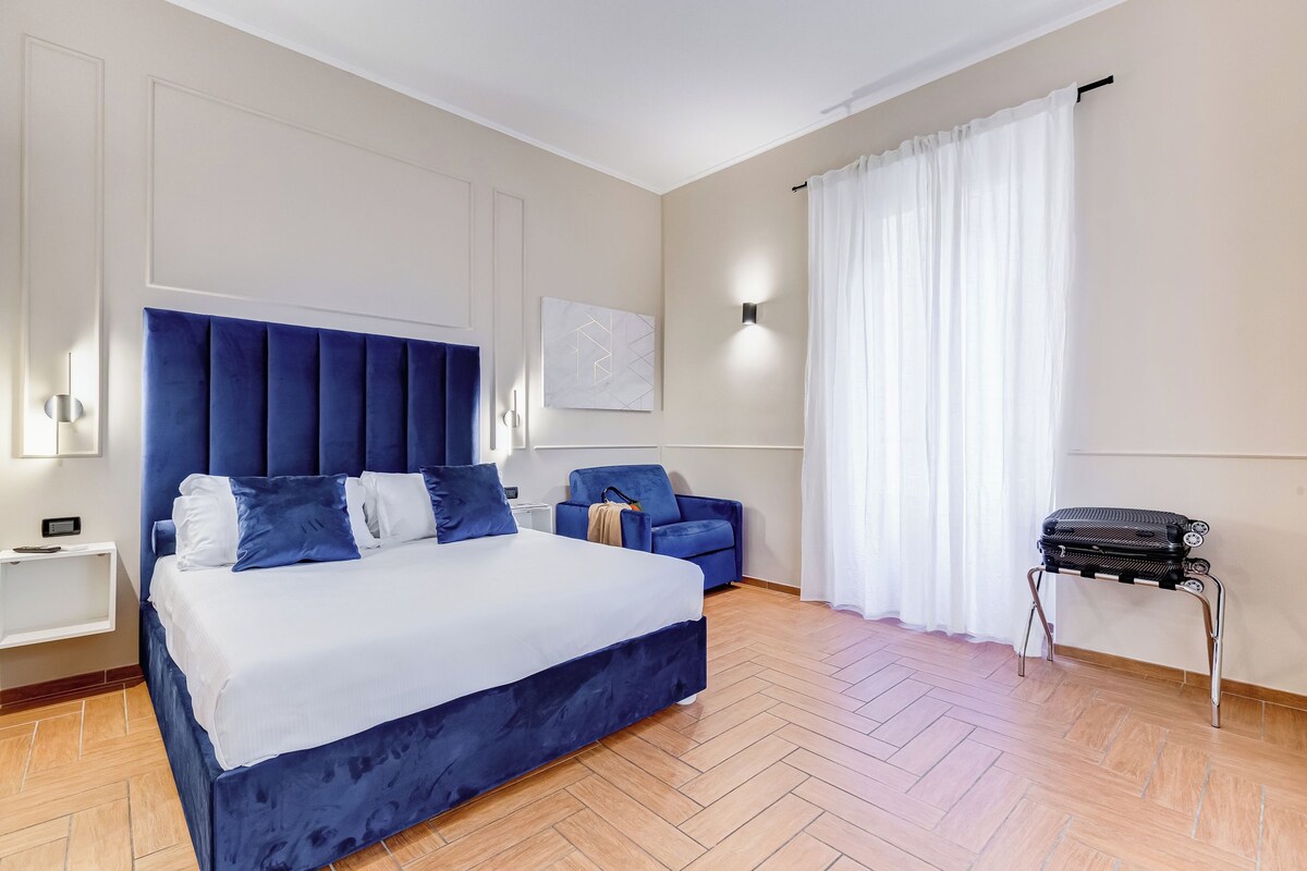 A modern hotel room with a large bed, a sofa, a small table, and a chair.