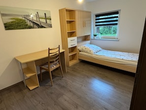 Ein Schlafzimmer mit einem Holztisch, einem Sessel, einem Bett mit einem Bettbezug mit Sternenmuster und einem Fenster mit Jalousien.