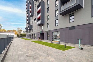 Un edifici modern amb teulada plana, múltiples balcons i un passeig pavimentat.