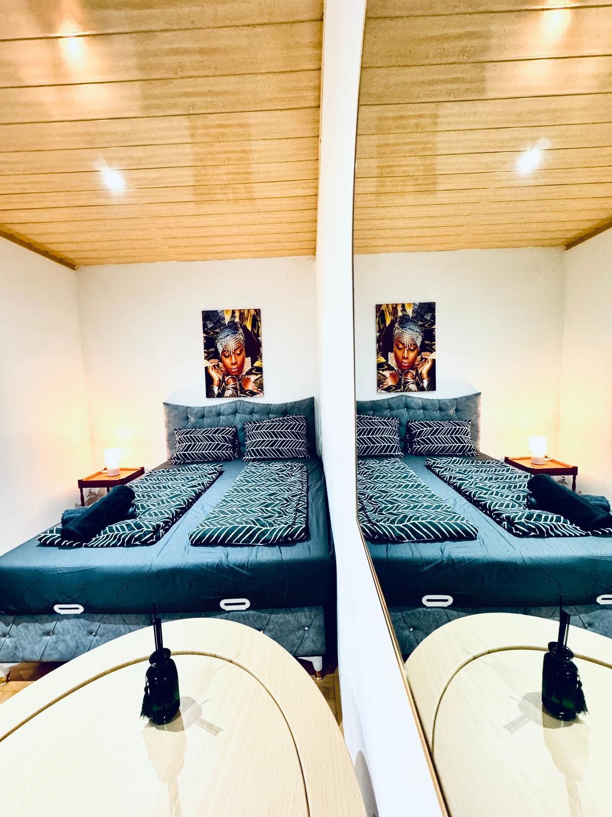 A mirrored view of a bedroom with a bed, pillows, a nightstand, and a wall-mounted artwork.