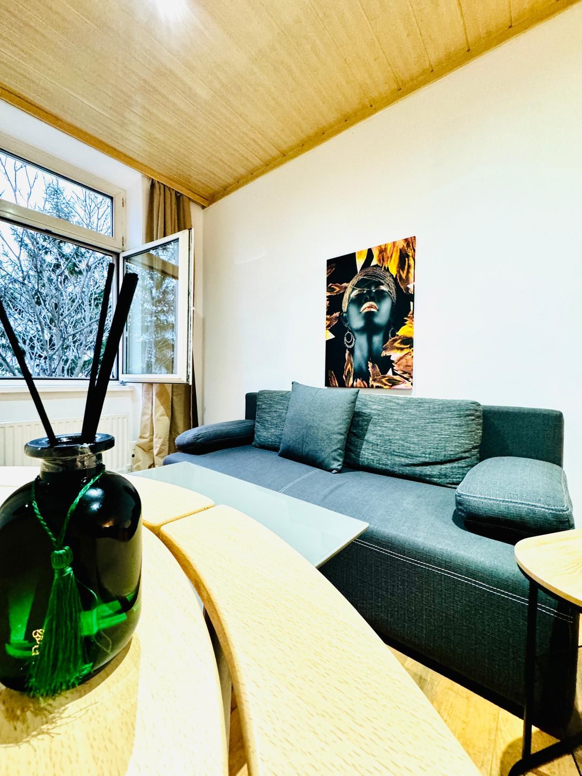 Een moderne woonkamer met een bank, een schilderij, een vaas en een raam met gordijnen.