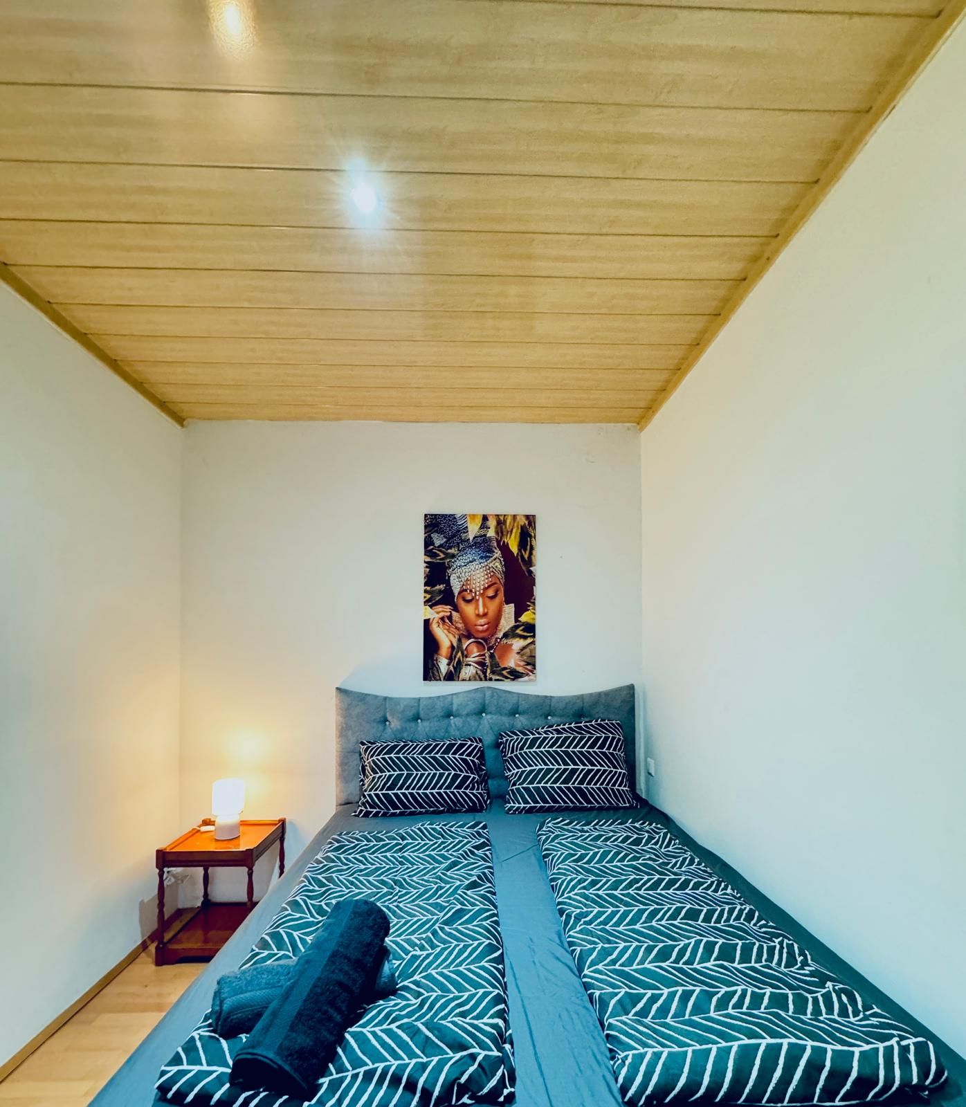 A bedroom with a bed, a nightstand, and a wall-mounted artwork.