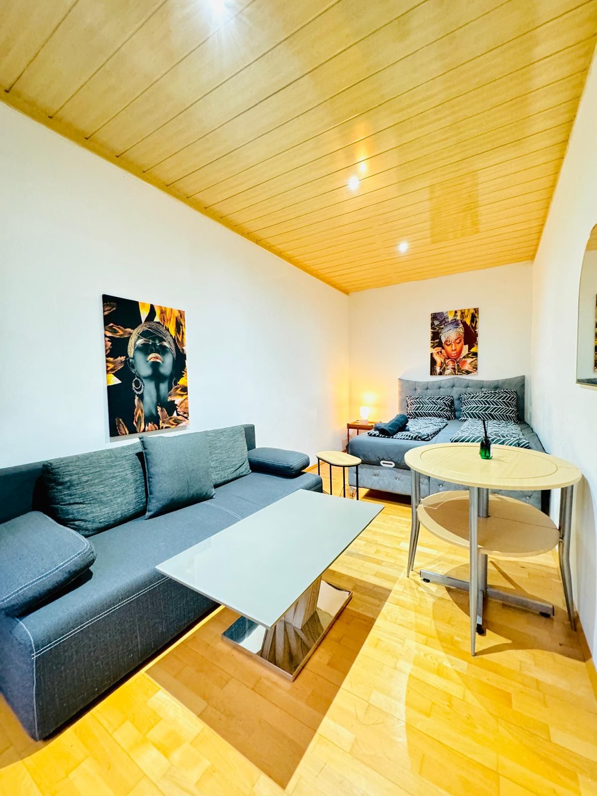 Een moderne woonkamer met een grijze bank, een klein rond tafeltje en kunstwerken aan de muren.