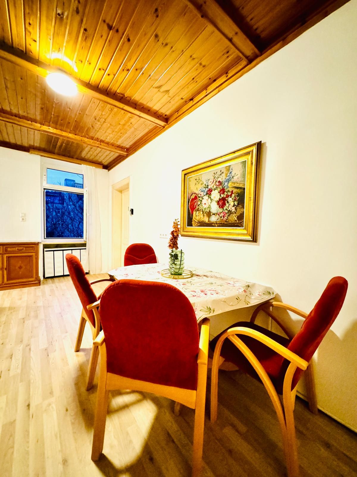 A dining area with a wooden ceiling, a table with a floral tablecloth, and red chairs.