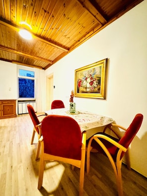A dining area with a wooden ceiling, a table with a floral tablecloth, and red chairs. - Vienna Stopover Private Room for Two (Wien)