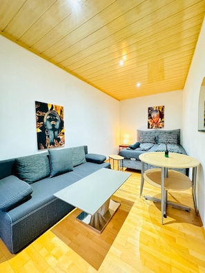 Una sala de estar moderna con un sofá gris, una pequeña mesa redonda y obras de arte en las paredes.