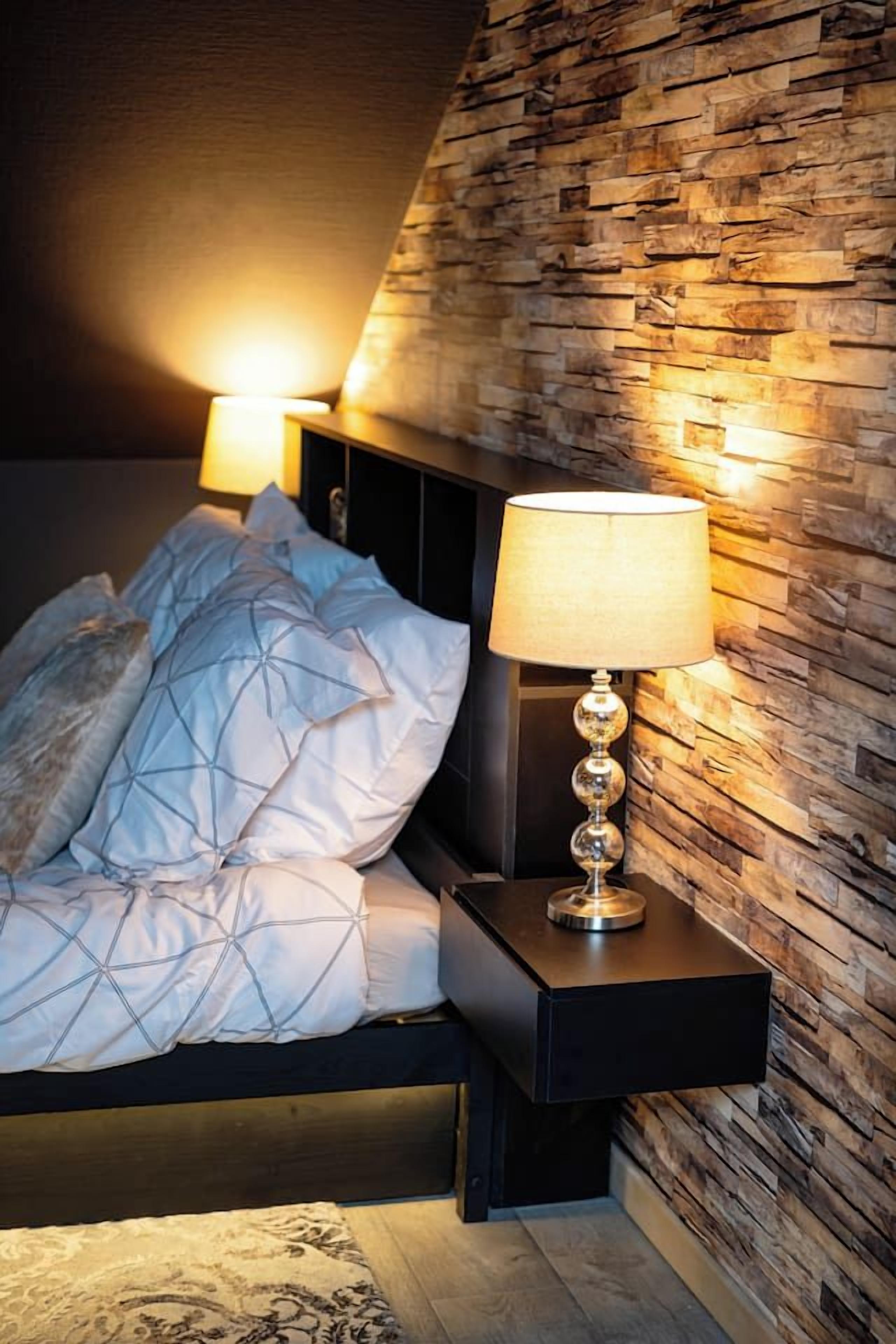Une chambre à coucher avec un lit, une table de chevet, une lampe et un mur à texture.