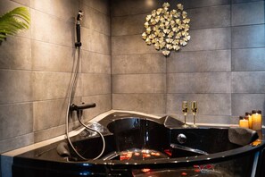 A modern bathroom with a black bathtub, a shower head, and a decorative wall piece.