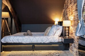 A bedroom with a bed, two bedside lamps, a wooden headboard, and a patterned rug.