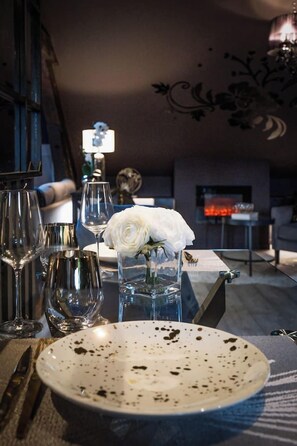 A dining table with a white plate, wine glasses, and a vase with a white flower.