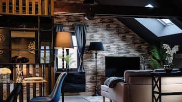 Un espace de vie de style loft avec des poutres apparentes, un mur en pierre, un canapé, un téléviseur et un coin repas comprenant une table et des chaises.