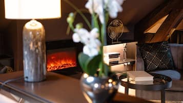 Un salon chaleureux avec une cheminée, une lampe, un vase rempli de fleurs et un canapé agrémenté de coussins à motifs.