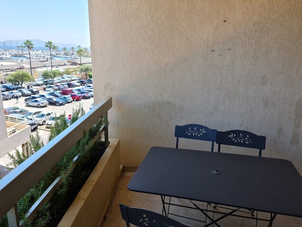 A balcony with a table and chairs, overlooking a parking lot and a marina with boats. - Charming Air-Conditioned Studio with Balcony, Steps from the Beach (Cavalaire-sur-Mer)