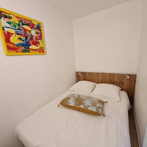 A single bed with white bedding and a decorative pillow, a wooden headboard, and a colorful painting on the wall. - Charming Air-Conditioned Studio with Balcony, Steps from the Beach (Cavalaire-sur-Mer)