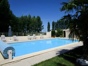 Una piscina con sillas de descanso y una sombrilla, rodeada de follaje y árboles.