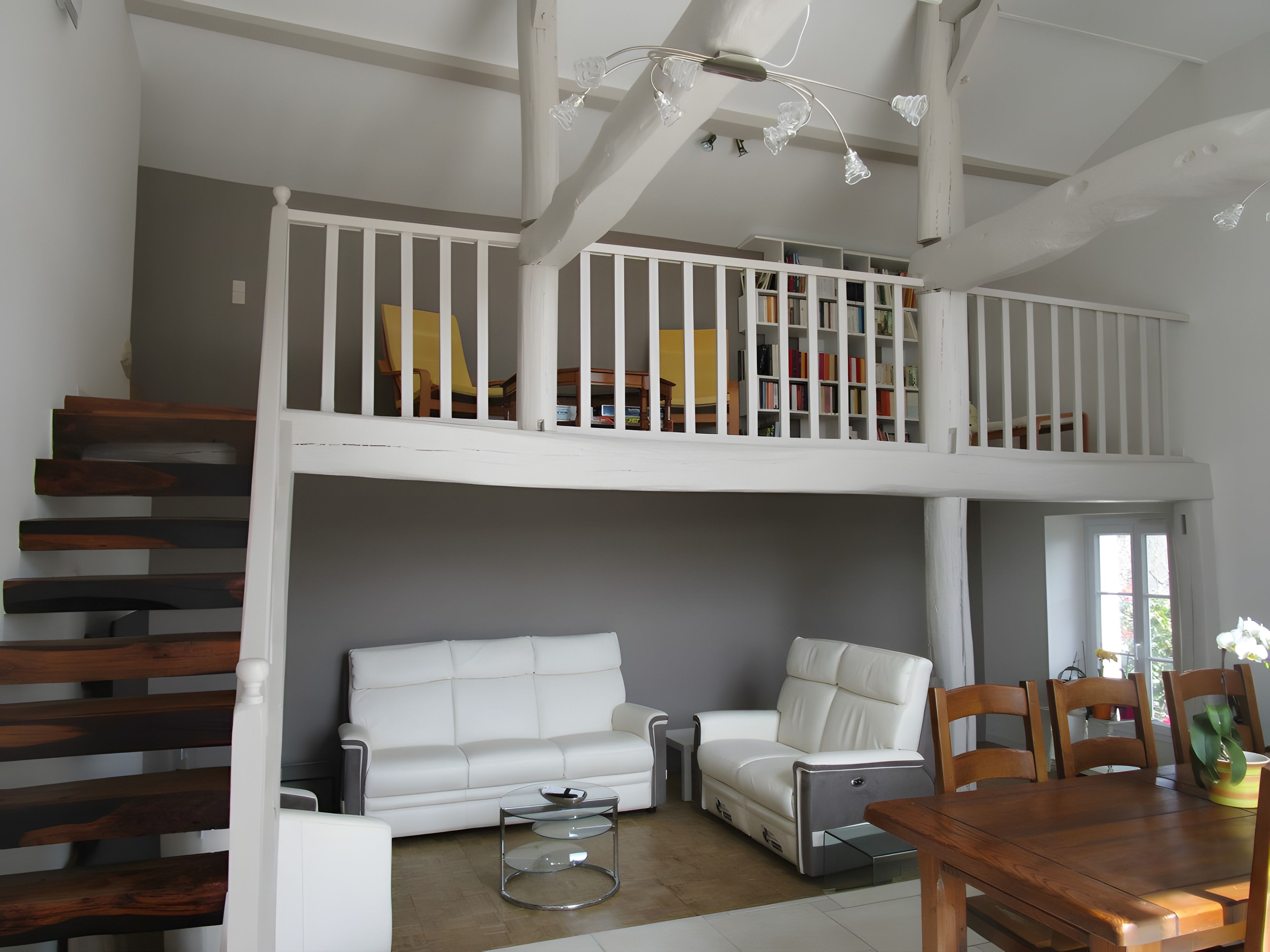 Ein mehrgeschossiges Wohnzimmer mit Treppe, weißen Möbeln und einem Balkon mit Bücherregalen.