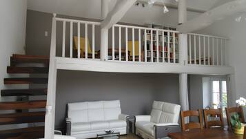 Ein mehrgeschossiges Wohnzimmer mit Treppe, weißen Möbeln und einem Balkon mit Bücherregalen.
