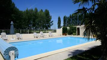 Ein Swimmingpool mit Liegestühlen und Sonnenschirm, umgeben von viel Grün und Bäumen.