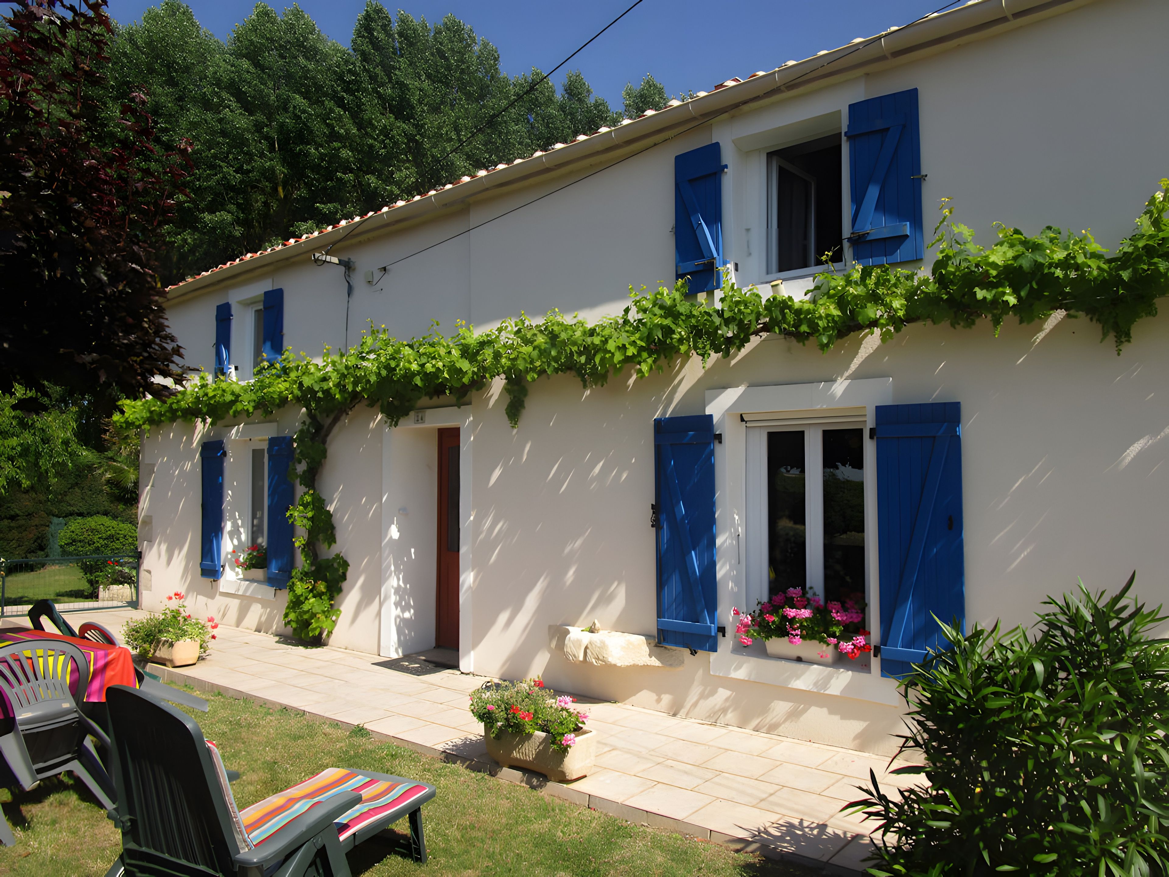 Une maison à deux étages avec des volets bleus, une porte d’entrée et un petit porche.