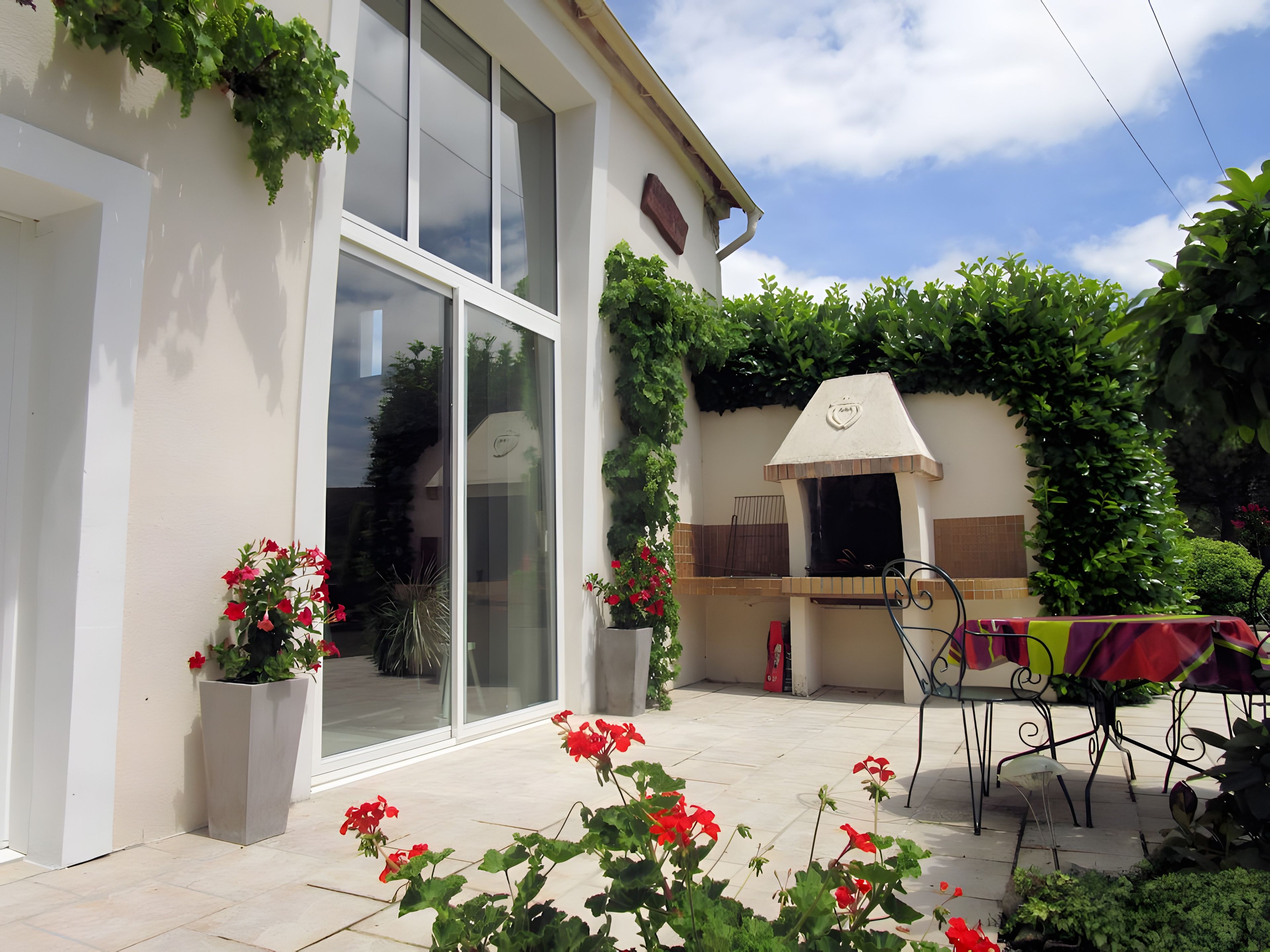 Ein modernes Haus mit Terrasse, Grill und Blumentöpfen.