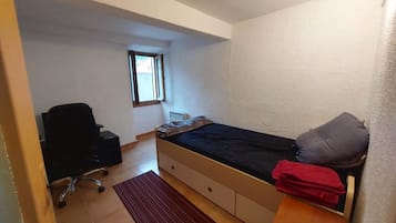 Een kleine kamer met een enkel bed, een raam, een bureau en een stoel.