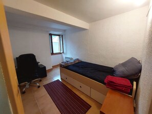 A small, single-bed room with a window, a desk, and a chair.