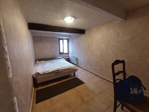 A small, narrow room with a single bed, a chair, and a window.