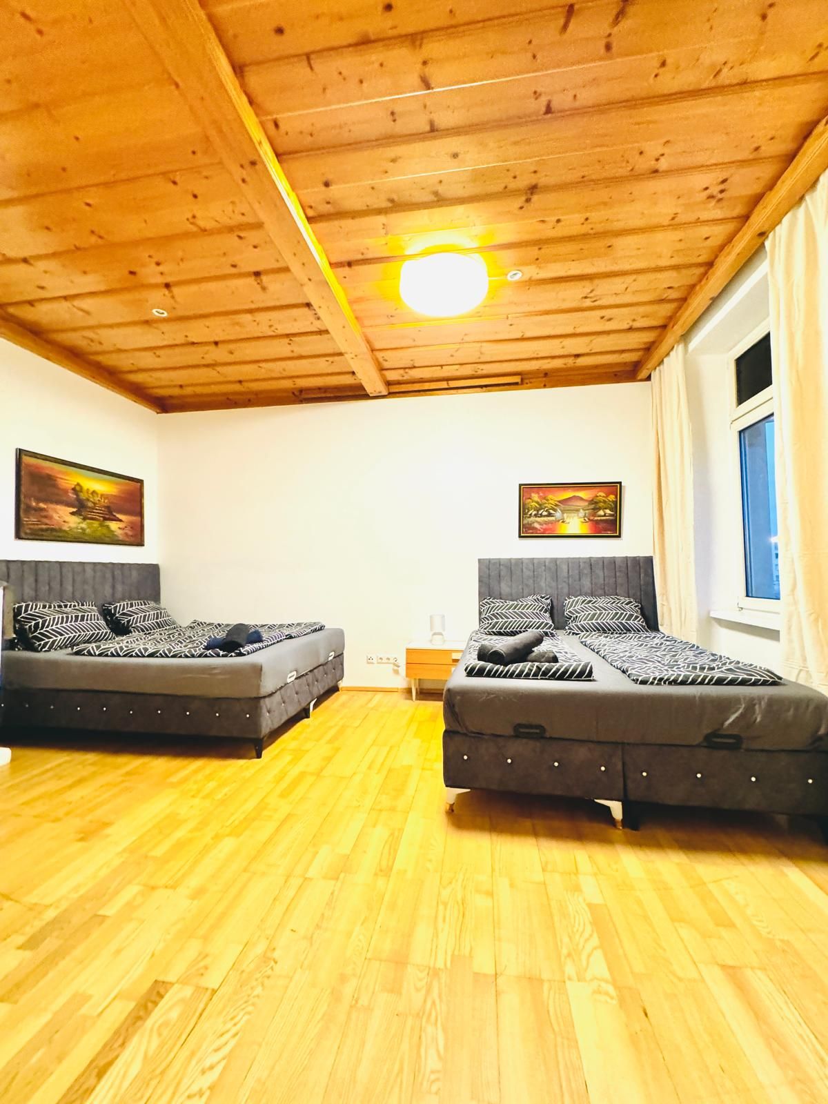 Een kamer met twee bedden, houten vloer, houten plafond en twee schilderijen aan de muur.