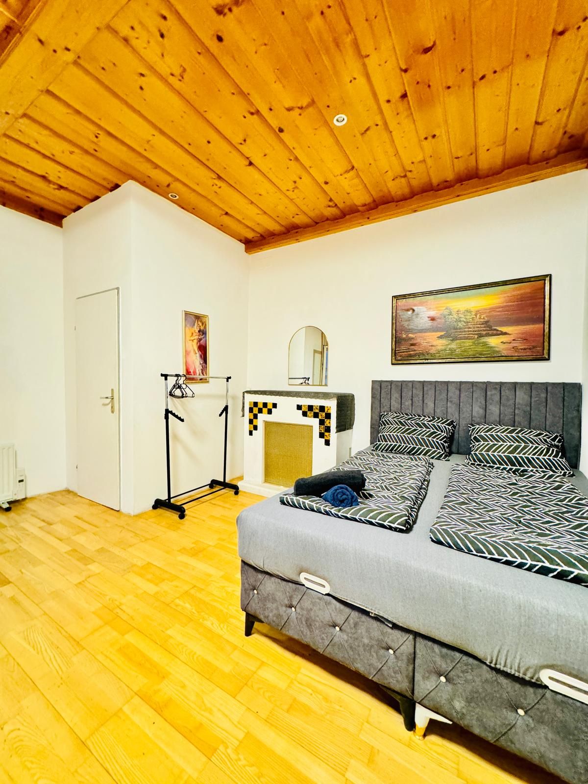 A bedroom with a bed, a dresser, a mirror, and a painting on the wall.
