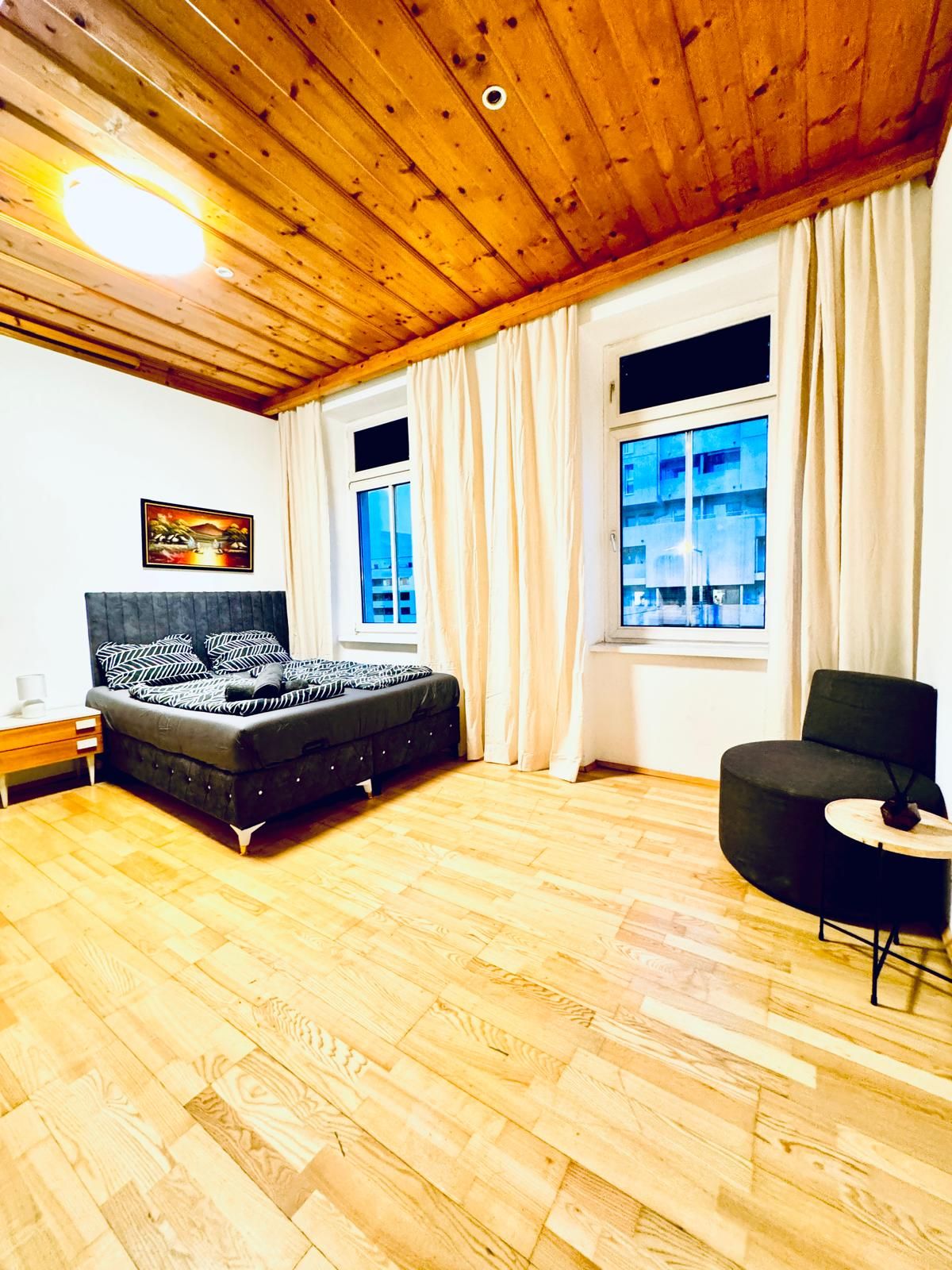 A room with a bed, a chair, a wooden floor, and a window with curtains.