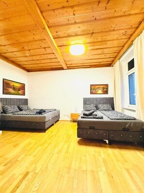 A room with two beds, wooden flooring, a wooden ceiling, and two paintings on the walls. - Vienna Basecamp Private Room (Wien)