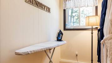 A laundry room with a hanging rack, an ironing board, and a lamp.