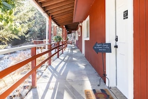 A covered outdoor corridor with a wooden railing, a signboard, and a door. - Aspen Song Mountain Retreat (Jefferson County)