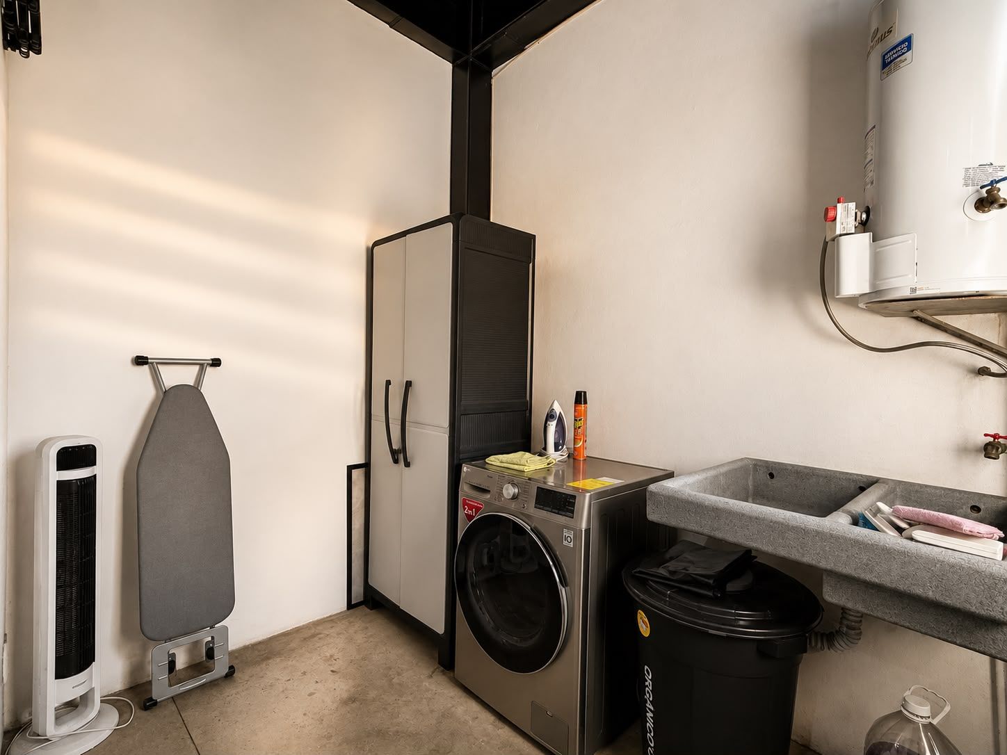 Une petite buanderie équipée d’un lave-linge, d’un sèche-linge, d’une planche à repasser et d’un chauffe-eau.