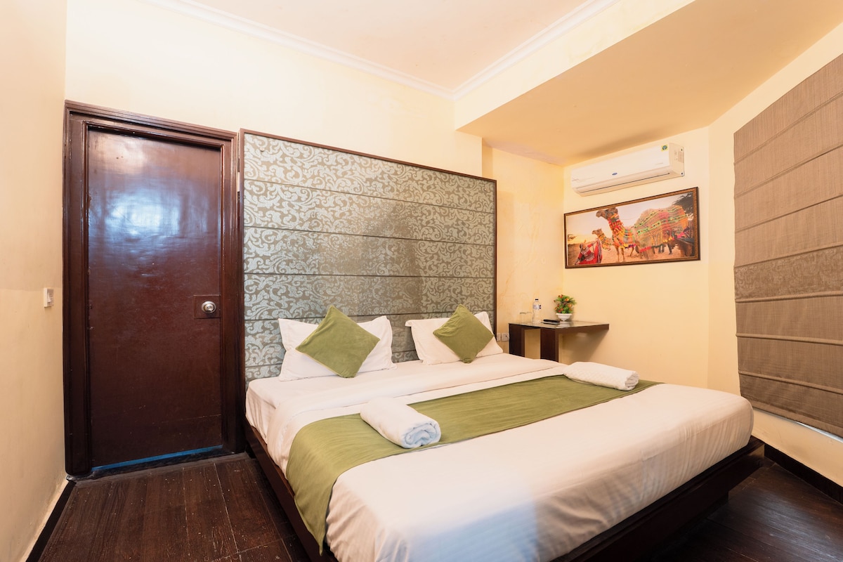 A hotel room with a bed, a door, a wall-mounted air conditioner, and a decorative wall panel.
