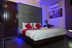 A hotel room with a bed, a nightstand, a wall-mounted air conditioner, and a framed picture. - Hotel Royal Primes (Jaipur)