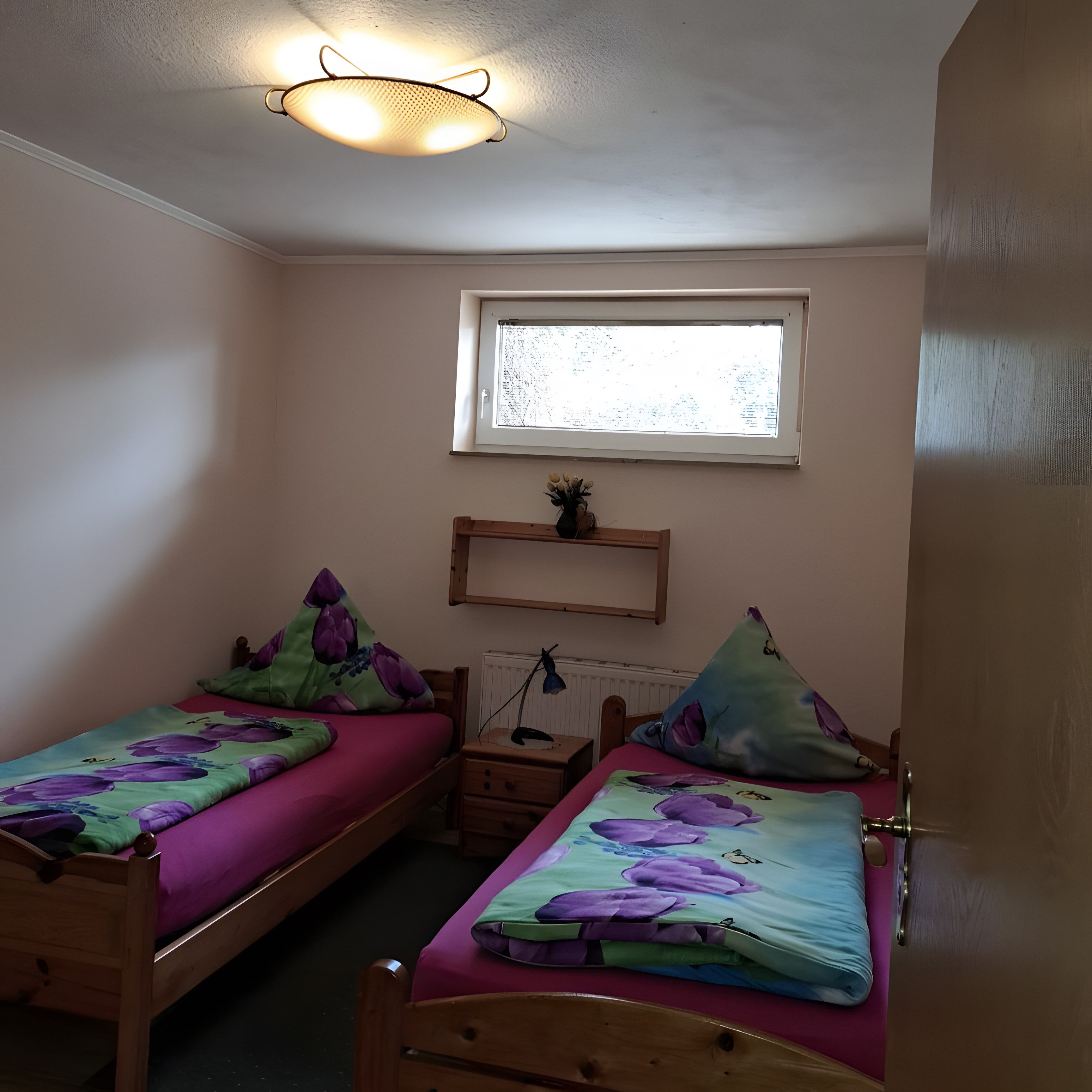 Ein Schlafzimmer mit zwei Einzelbetten, einem Fenster, einem Regal und einer Tür.